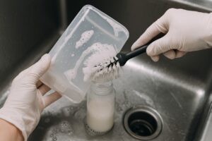 Close-up of a cafeteria worker cleaning and sanitizing the detachable nozzle of a commercial milk dispenser machine for daily food safety.
