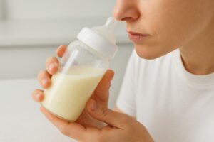 A mother gently swirling a bottle of breast milk while smelling it carefully on a clean kitchen counter, avoiding shaking.