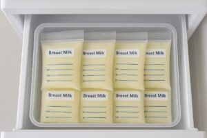 An overhead view of several flat-frozen breast milk bags neatly stacked vertically inside a clear freezer storage bin or basket.