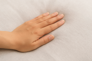 A close-up of a hand gently performing a downward stroke or light compression on a soft, padded surface, illustrating a technique to encourage fluid flow.