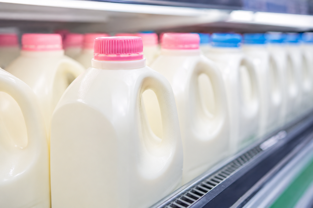 A row of milk jugs in a grocery store focusing on the pink cap of fat free skim milk.