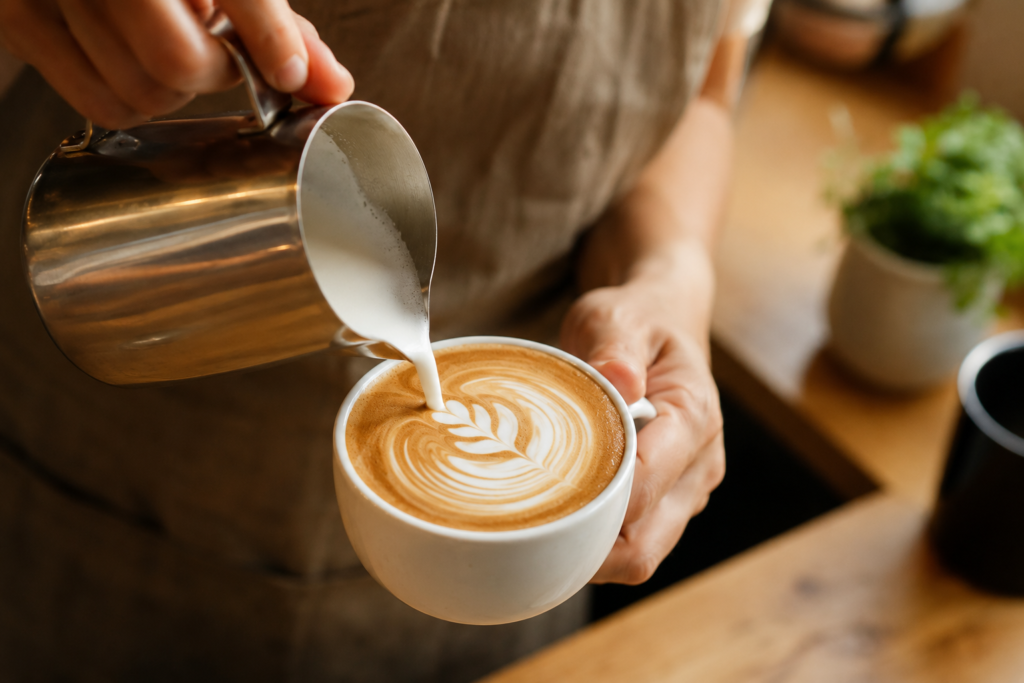 Steamed plant based milk being poured into a hot cup of espresso coffee to make a latte.