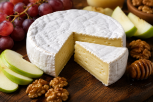 Fresh wheel of French brie cheese with a wedge cut out on a wooden charcuterie board with fruit.
