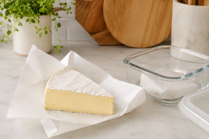 How to store brie cheese properly using cheese paper and glass container on a kitchen counter.