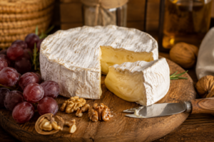 A wheel of homemade brie cheese cut open on a wooden board with grapes