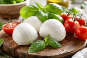 Fresh mozzarella cheese balls on wooden board with basil and cherry tomatoes.