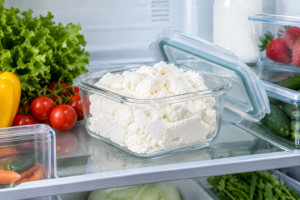 Fresh white ricotta cheese stored in a clear glass container inside a refrigerator.